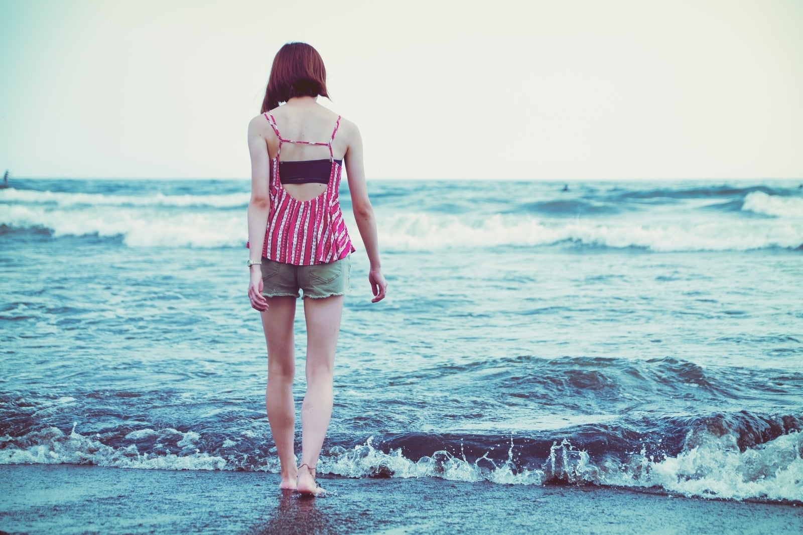 「波打ち際を裸足で歩く若い女性」の写真