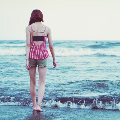 波打ち際を裸足で歩く若い女性の写真