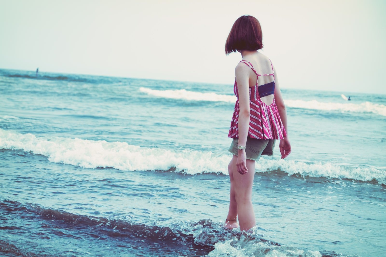 「海の波と浅瀬を歩く若い女性」の写真