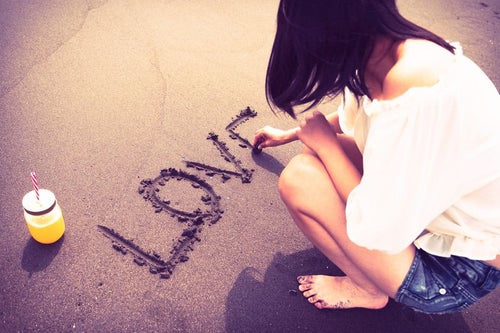 砂の上にLOVEと文字を書く女性のうしろ姿の写真