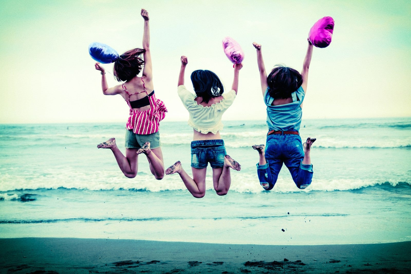 「波打ち際でジャンプするハッピーな若い女性三人組」の写真