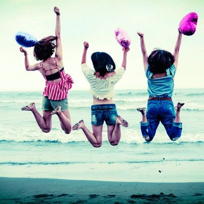 波打ち際でジャンプするハッピーな若い女性三人組の写真