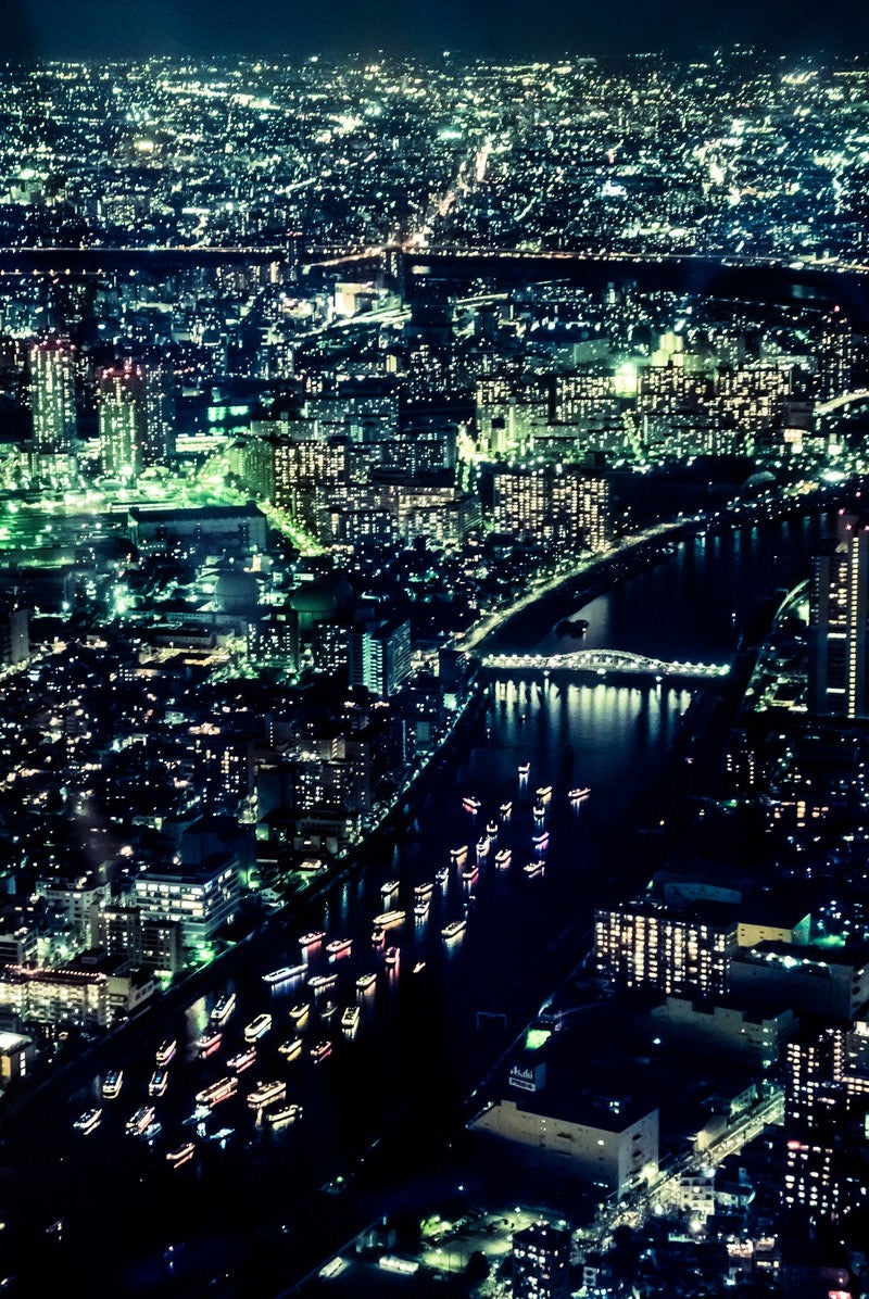 「川を流れるカラフルな屋形船と都会の夜景」の写真