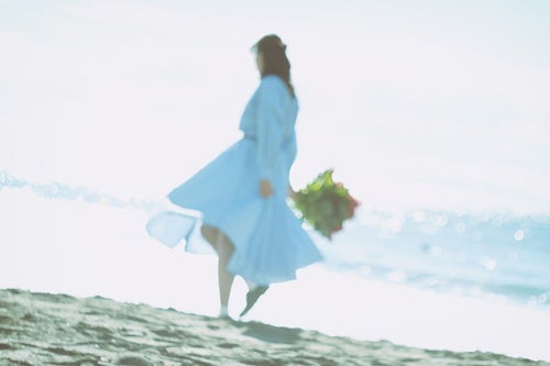 波打ち際を歩くスカートの女性の写真