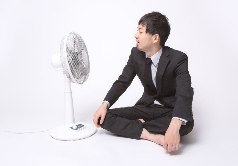 扇風機の前で涼もうとするサラリーマンの写真