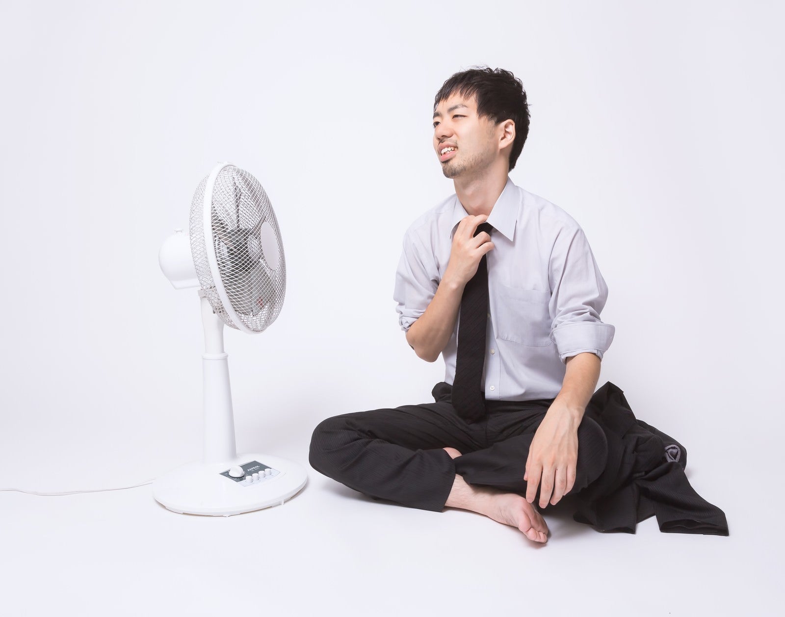 「暑すぎて上着を脱いで扇風機に当たる会社員」の写真［モデル：ひろゆき］