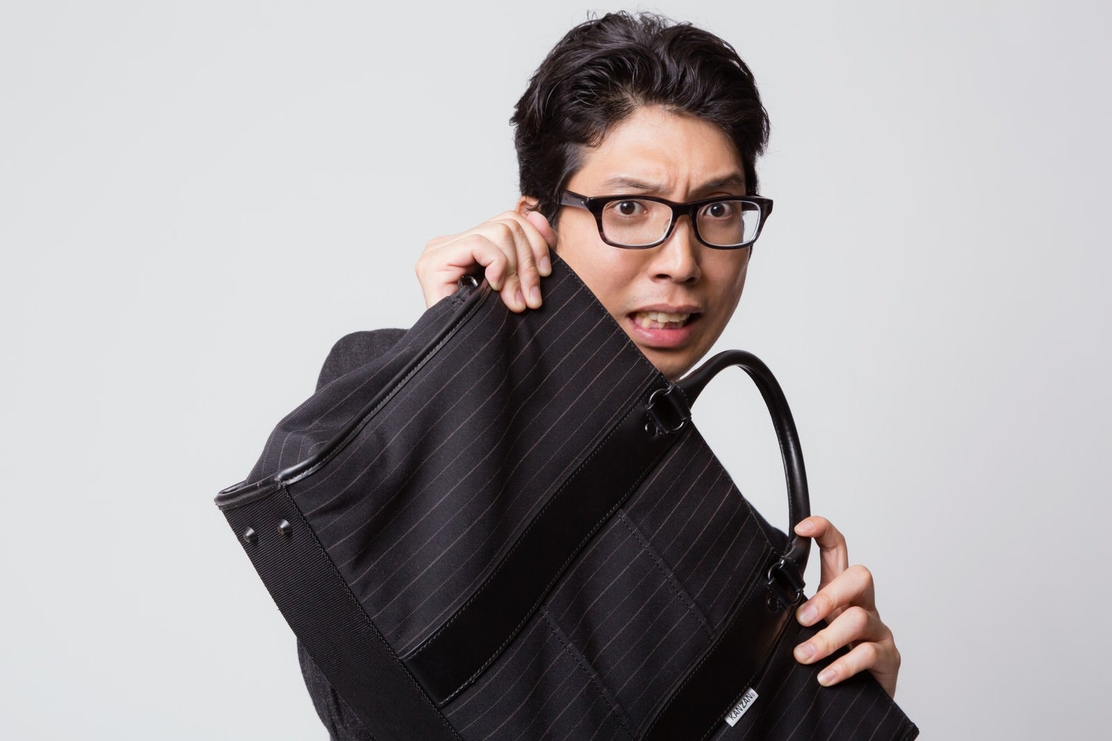 「鞄でガード（防御）する怯えた表情のビジネスマン」の写真［モデル：紳さん］