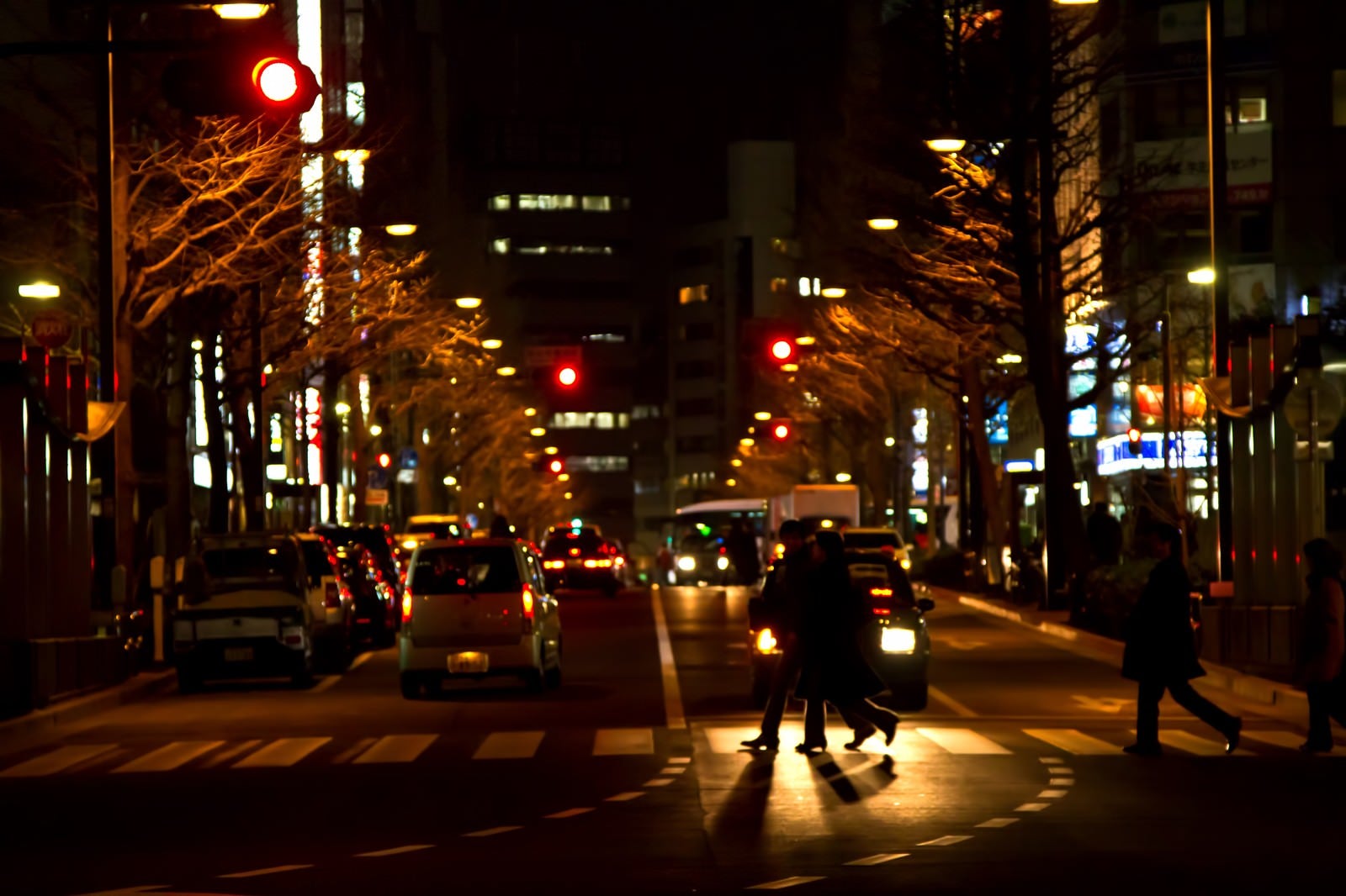 「夜、大通りの横断歩道を渡る人」の写真
