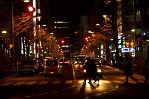 夜、大通りの横断歩道を渡る人の写真