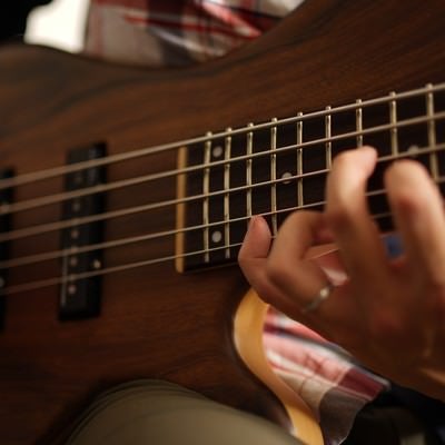 木目調のエレキベースを弾く男性ミュージシャンの手元アップの写真