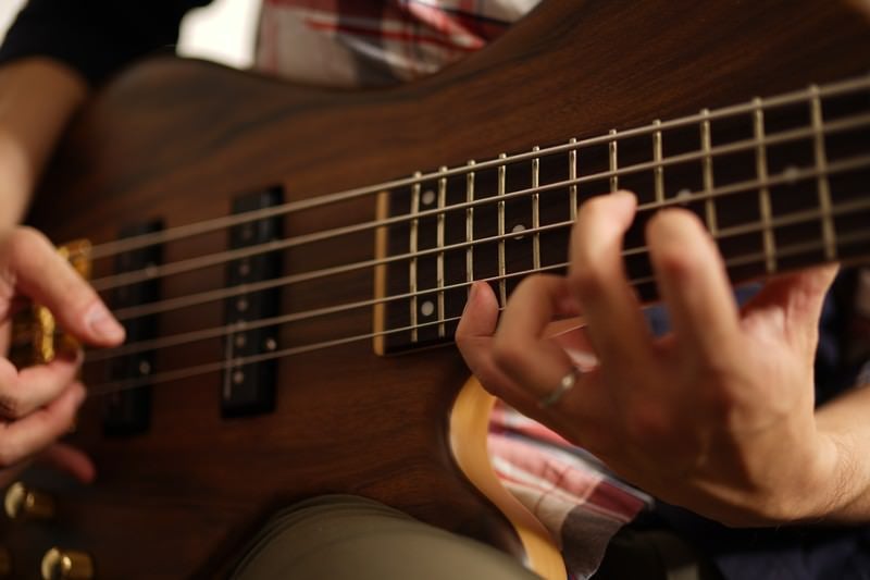 Close-up of a Male Musician's Hands Playing a Wood-Grain Electric Bass