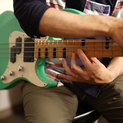 チェックシャツを着た男性が緑色のエレキベースを弾いている様子の写真