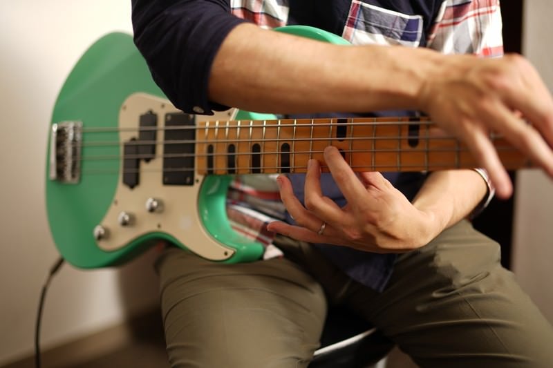 A man in a checkered shirt playing a green electric bass