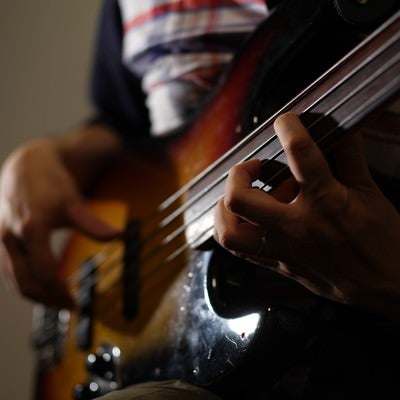 暗い照明の中でベースギターの弦を丁寧に押さえる演奏者の手元の写真