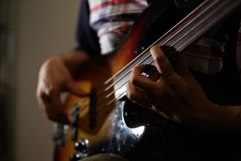 暗い照明の中でベースギターの弦を丁寧に押さえる演奏者の手元の写真