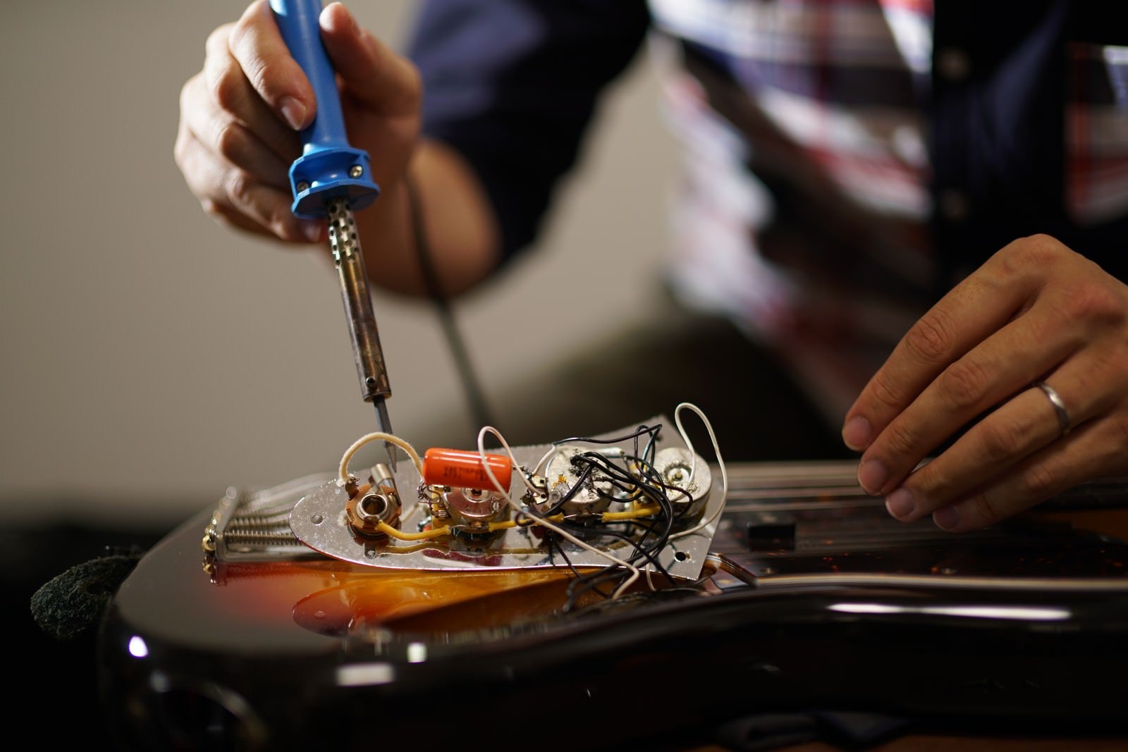 「ピックガードを外したエレキベースの電子部品をメンテナンスする作業風景」の写真