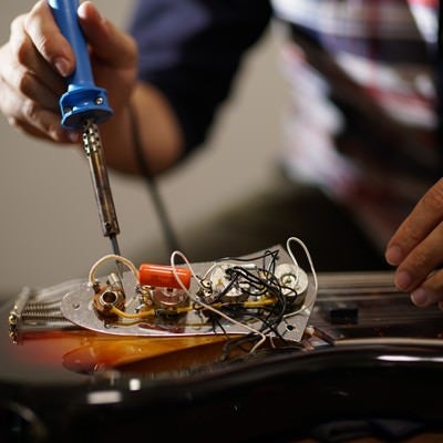 ピックガードを外したエレキベースの電子部品をメンテナンスする作業風景の写真