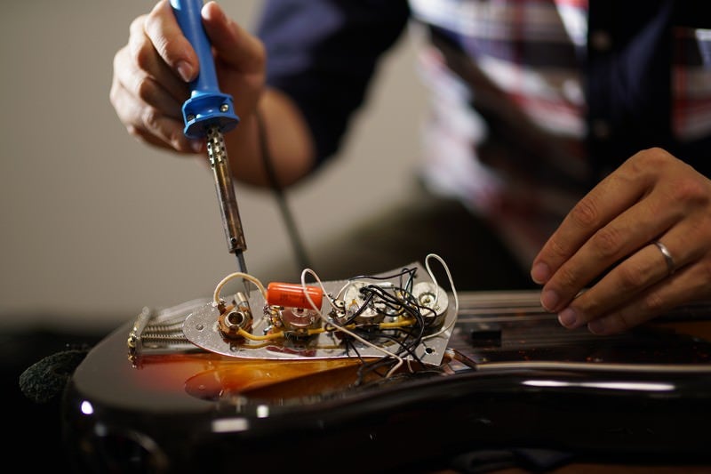 ピックガードを外したエレキベースの電子部品をメンテナンスする作業風景の写真