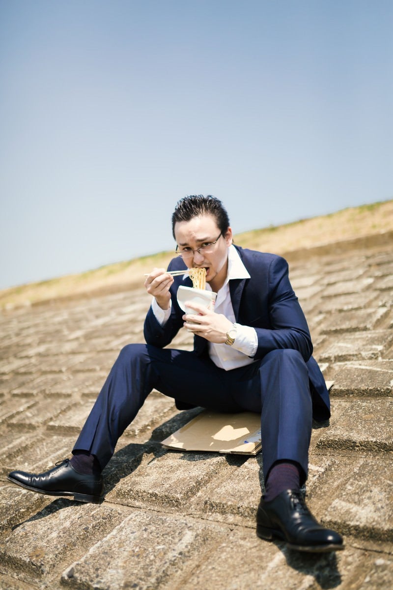 「土手で昼食を済ます営業中のビジネスマン」の写真［モデル：Max_Ezaki］