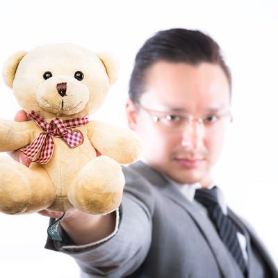 熊のぬいぐるみを差し出す外資系ビジネスマンの写真