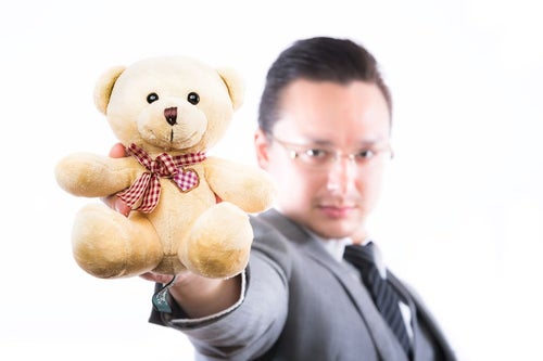 熊のぬいぐるみを差し出す外資系ビジネスマンの写真