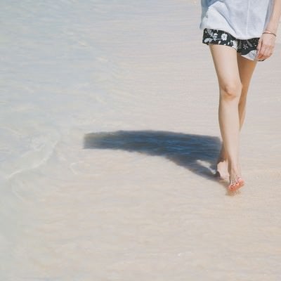 日傘をさして砂浜を歩く女性の足元の写真