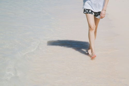 日傘をさして砂浜を歩く女性の足元の写真