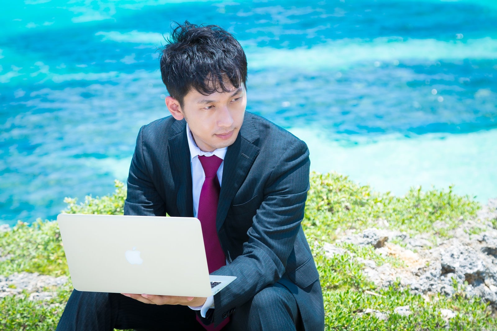 「青い海をバックにMBAで作業を行うビジネスマン」の写真［モデル：大川竜弥］