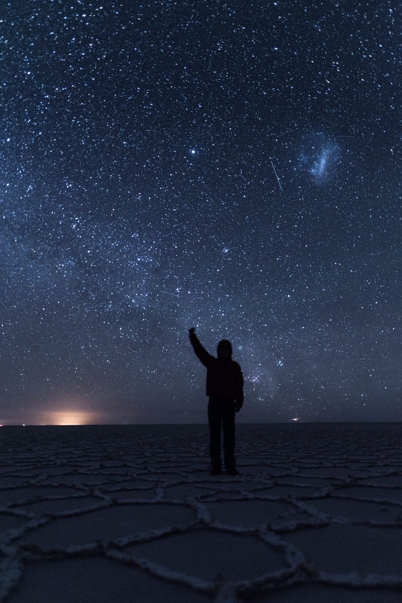 「ウユニ塩湖の星空の下で手をあげる観光客」の写真