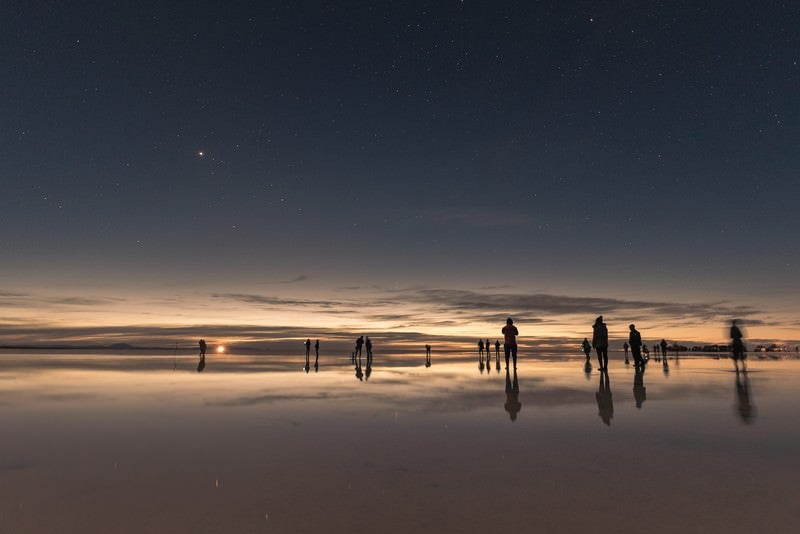 ウユニ塩湖の日没と星空を楽しむ観光客の写真
