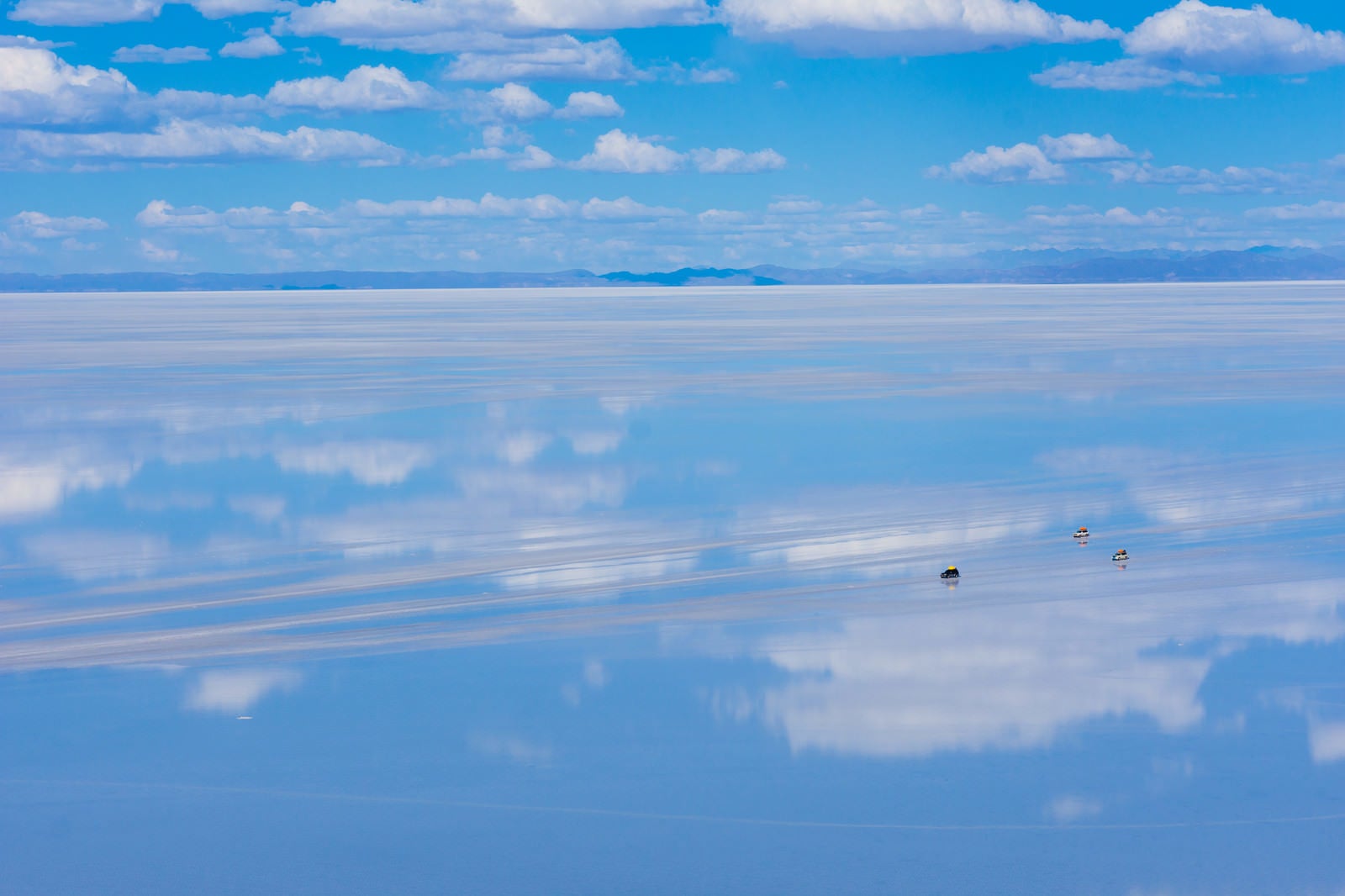 「天空の鏡と呼ばれる雨季のウユニ塩湖を横断する車」の写真