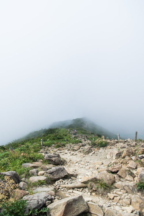 視界不良の雲の中へと進む登山者の写真