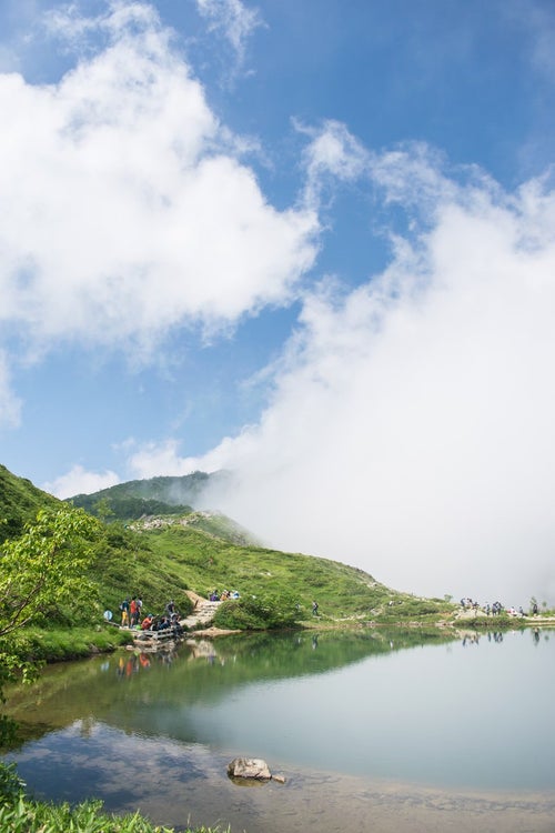 湖面に映る雲と登山者の写真
