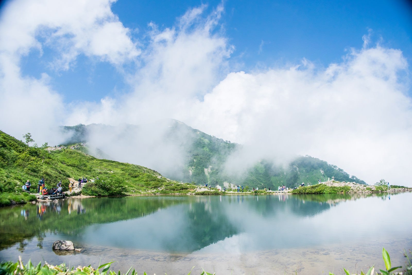 「湖面に映り込む雲と休憩中の登山者」の写真