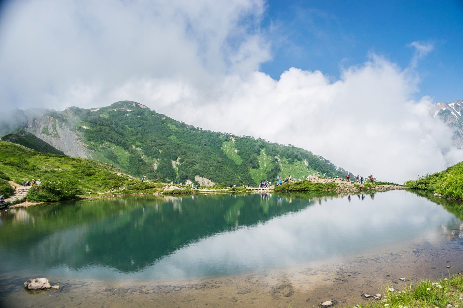 「湖畔で休む登山者と水鏡に映る山」の写真