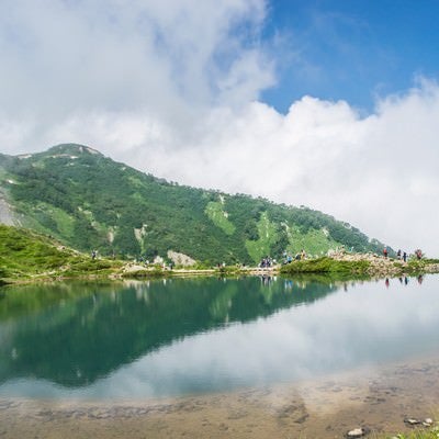 湖畔で休む登山者と水鏡に映る山の写真