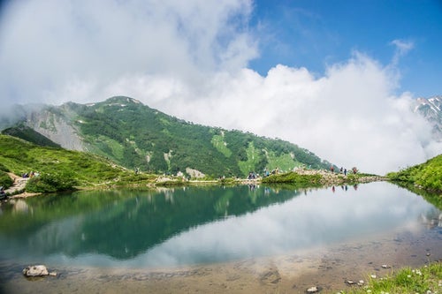 湖畔で休む登山者と水鏡に映る山の写真