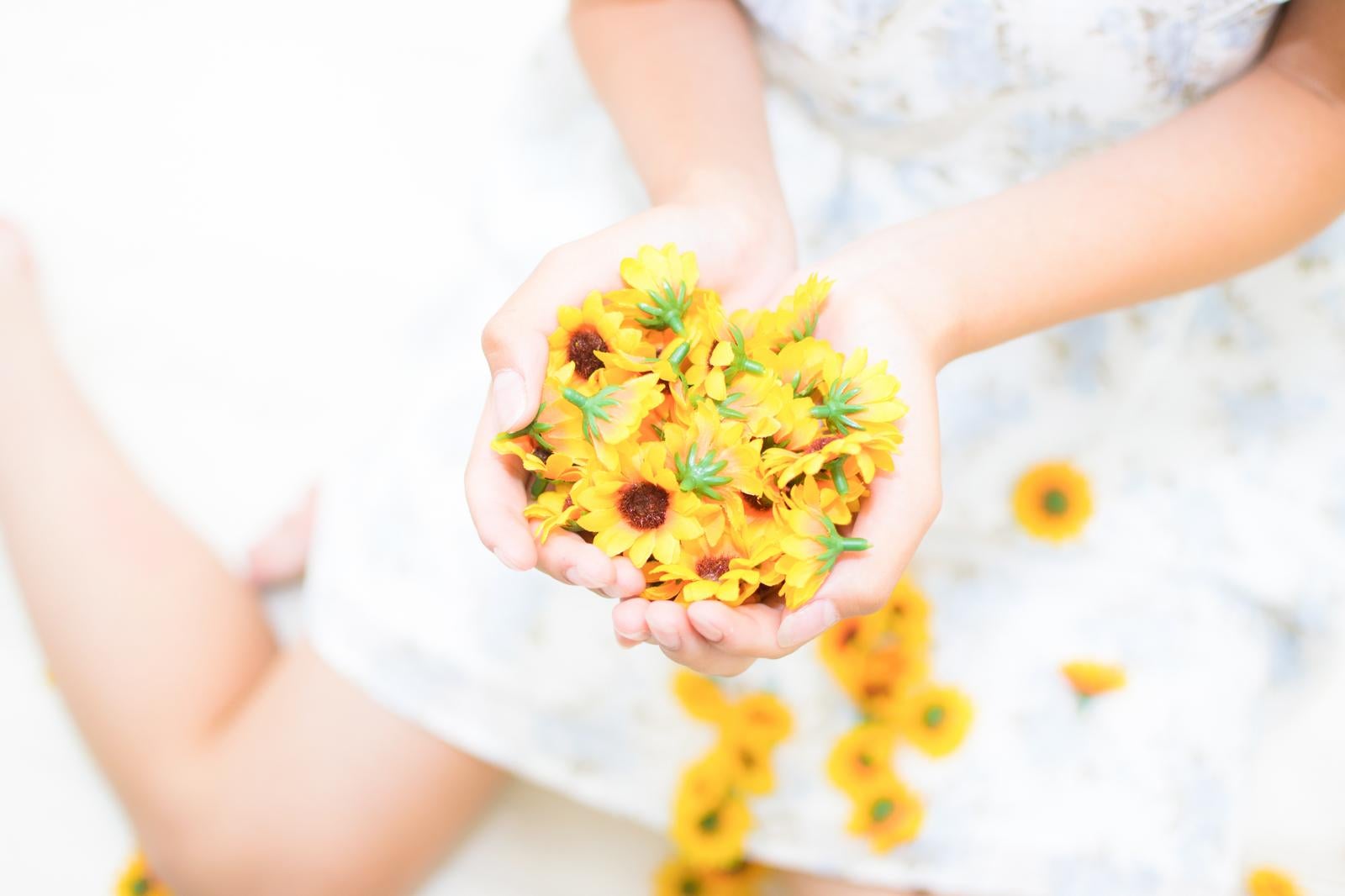 「小さな黄色いひまわりの造花を両手で包み込む女性」の写真