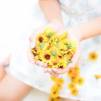 小さな黄色いひまわりの造花を両手で包み込む女性の写真