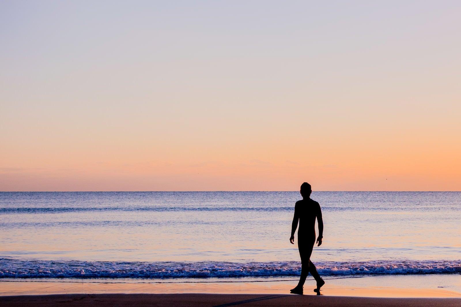 「夕暮れの砂浜を歩く男性のシルエット」の写真