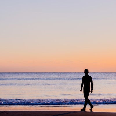 夕暮れの砂浜を歩く男性のシルエットの写真