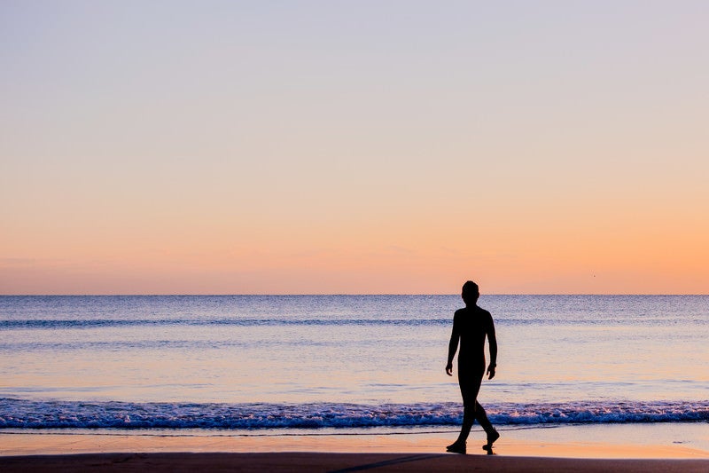 夕暮れの砂浜を歩く男性のシルエットの写真