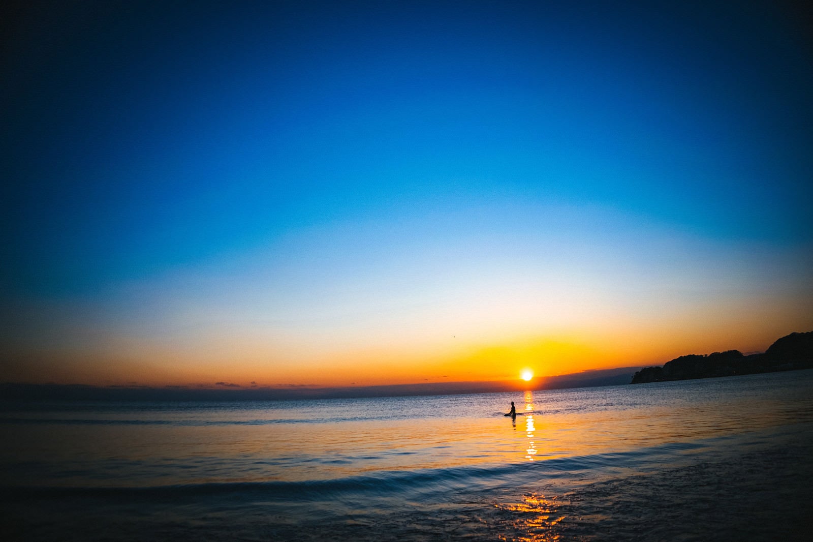 「夕日の焼けた海に浮かぶサーファー」の写真