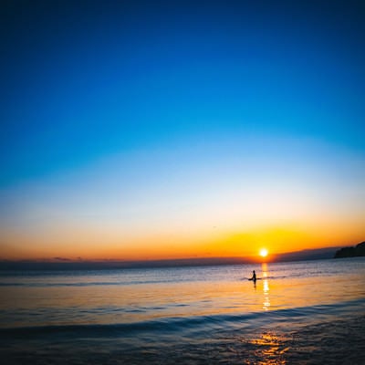 夕日の焼けた海に浮かぶサーファーの写真