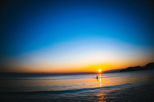 夕日の焼けた海に浮かぶサーファーの写真