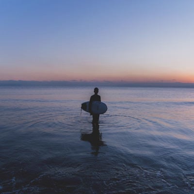 日没の海に佇むサーファーの男性の写真