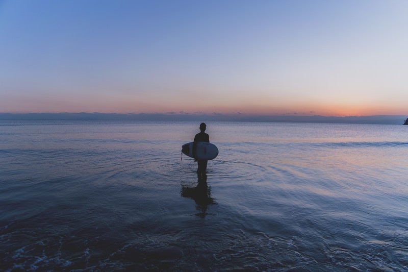 日没の海に佇むサーファーの男性の写真