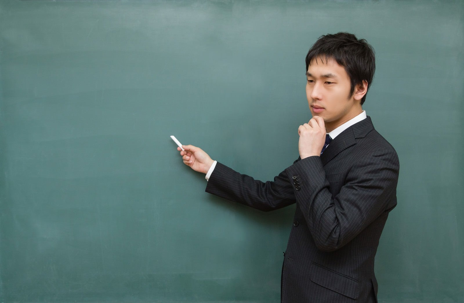 「黒板に向かって考えてしまう先生」の写真［モデル：大川竜弥］