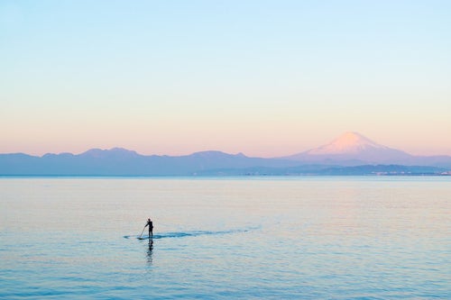 富士山をバックにスタンドアップパドルボードを楽しむ男性の写真