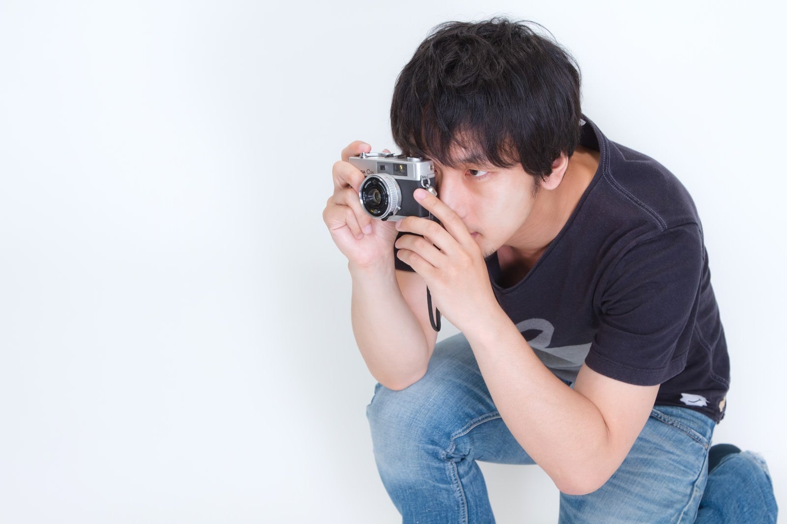 「しゃがみこんでカメラを構える男性」の写真［モデル：大川竜弥］